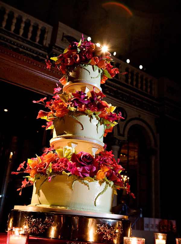 tall tiered white wedding cake with purple roses, and orange, bright red, and chartruese flowers - photo by Maloman Photographers